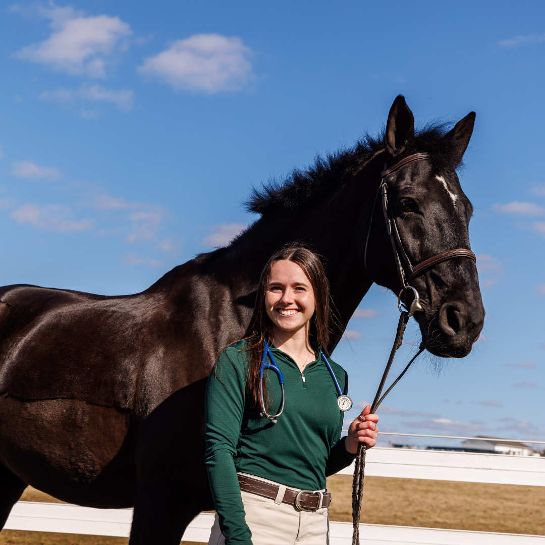 Nina Dellarte is smiling next to a dark horse on DelVal's campus. 