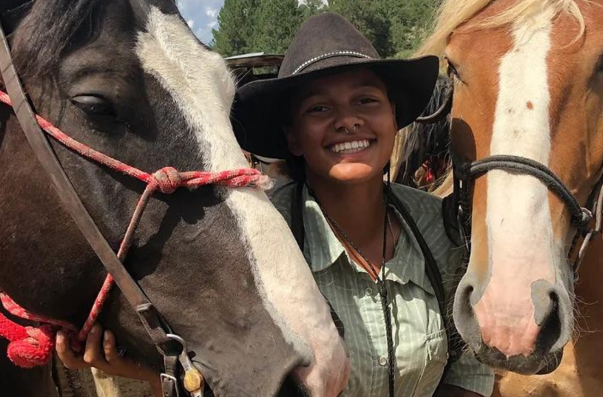 An Alumna is smiling while standing with two horses beside her. 