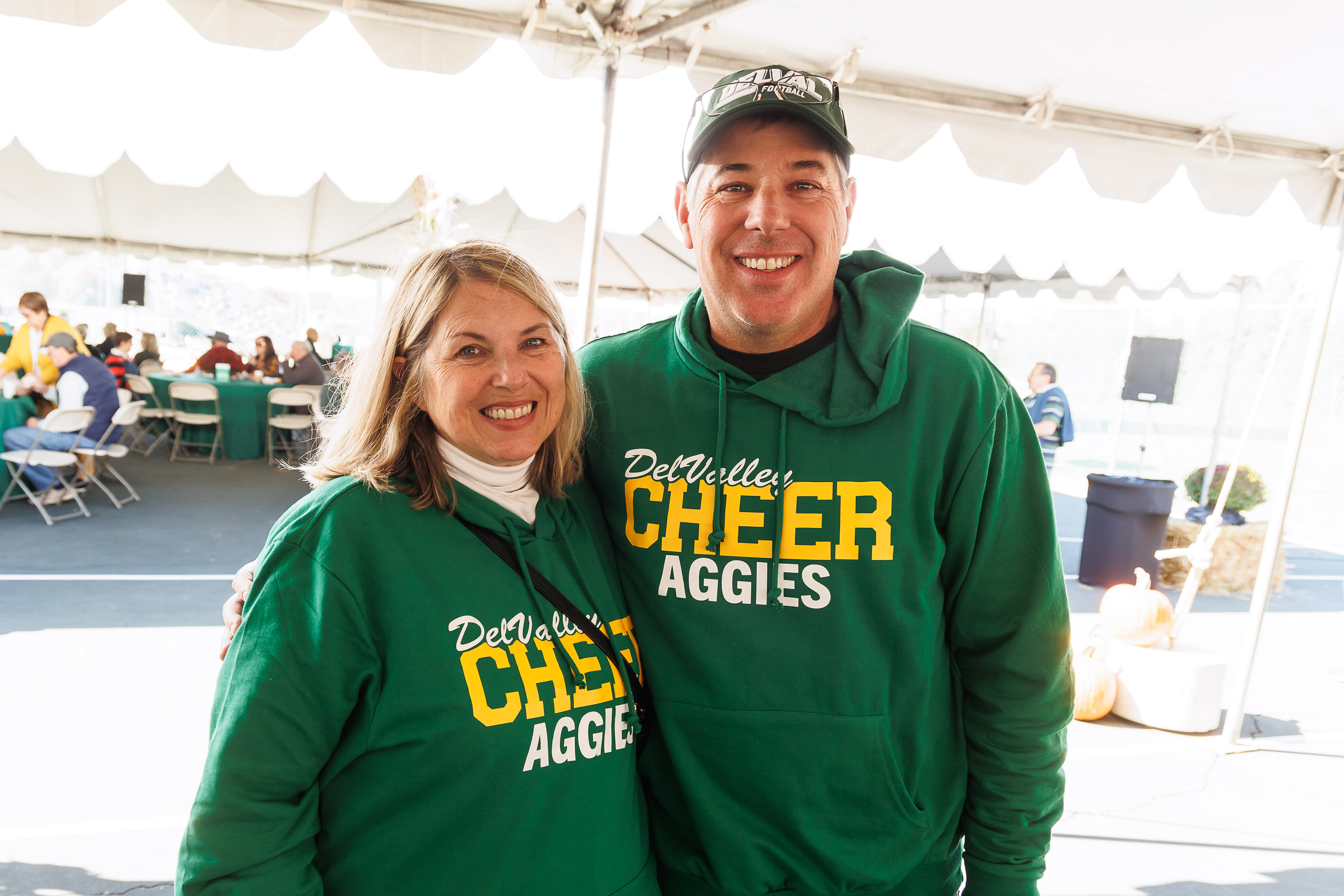 One alumnus and alumna are wearing delval cheer sweatshirts are next to eachother smiling at the camera. 