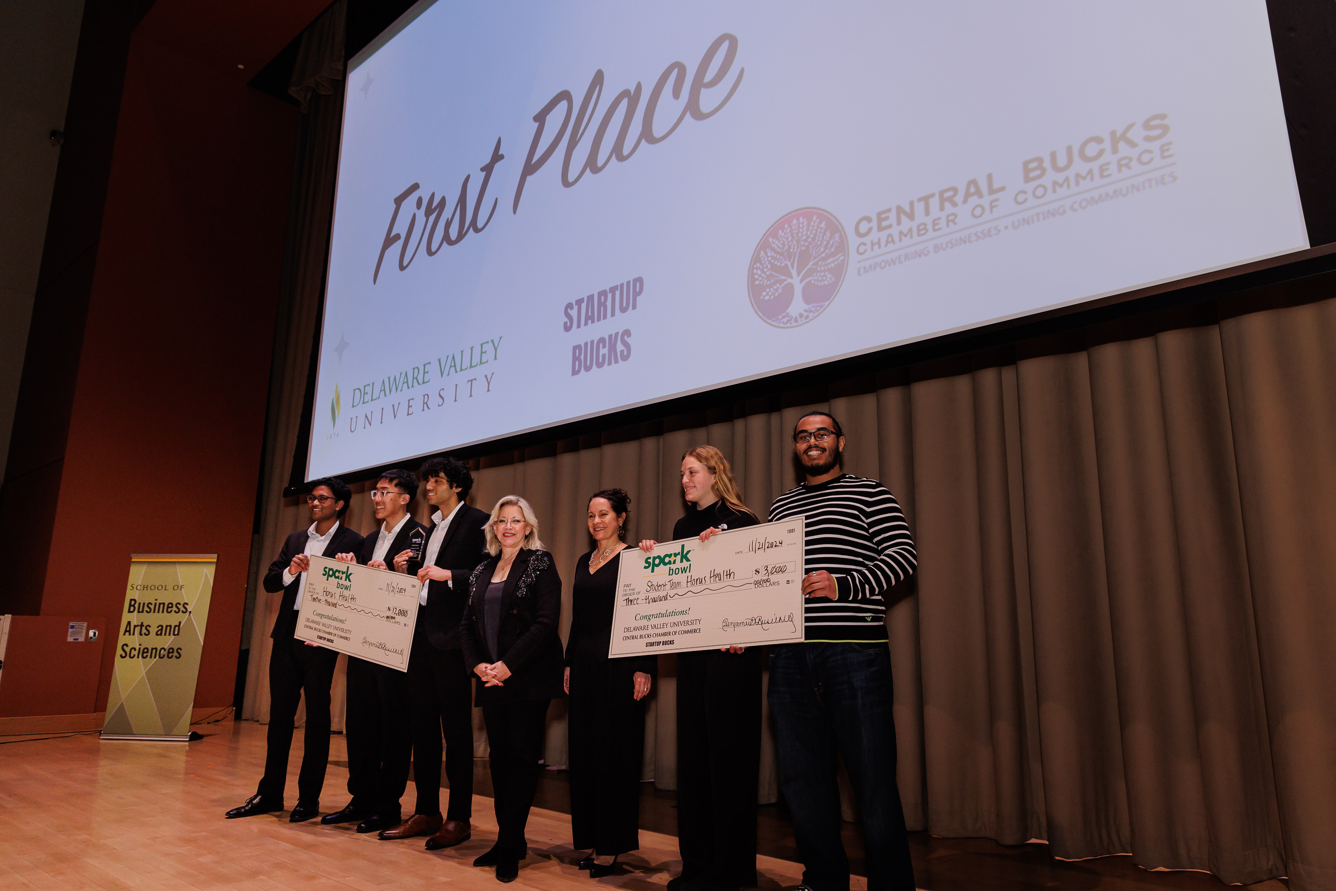 Spark Bowl Winners, Horus Health are on stage with their student team holding giant checks.