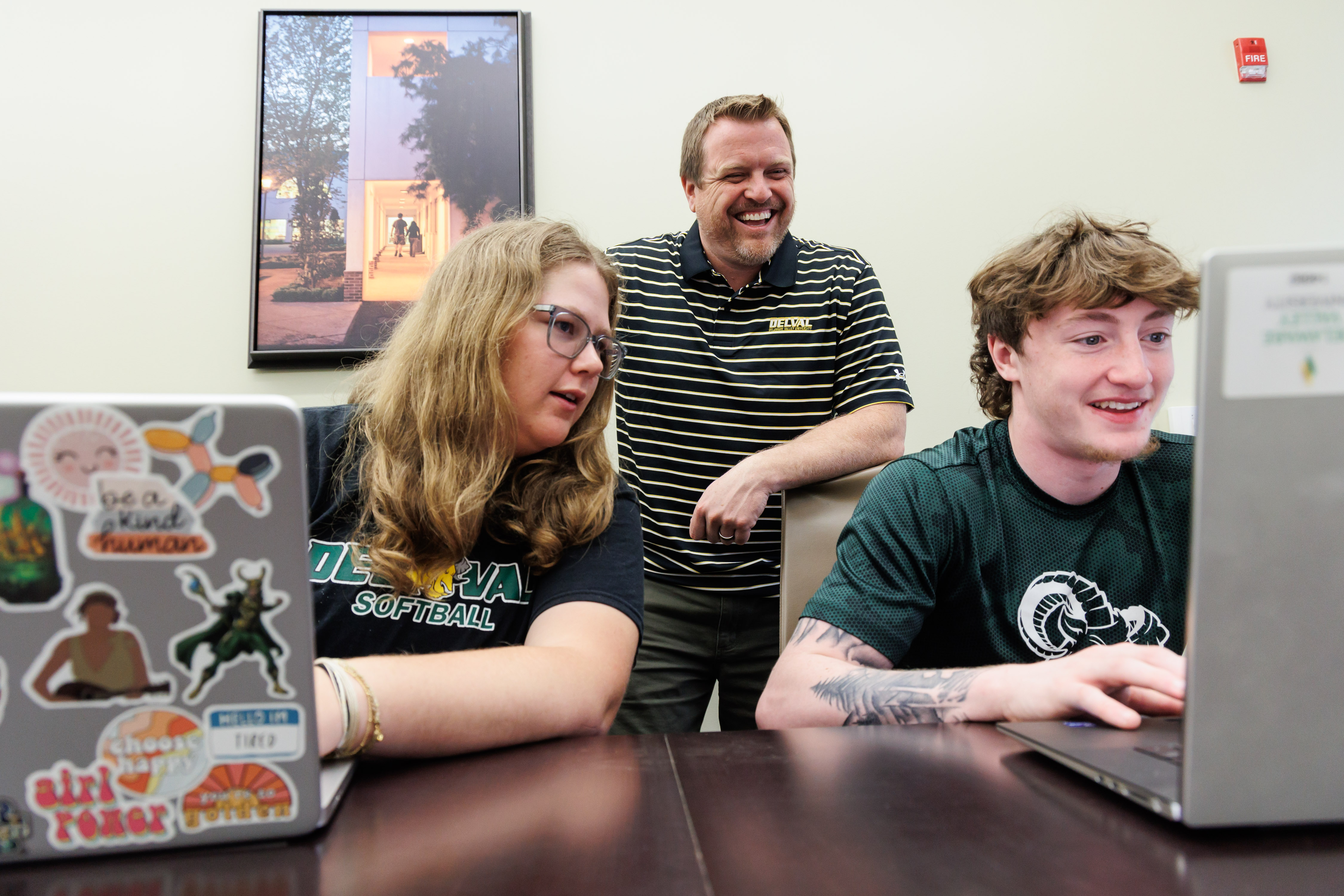 Jeff Wehrung, Business Faculty is helping two students on their laptops at a conference table.