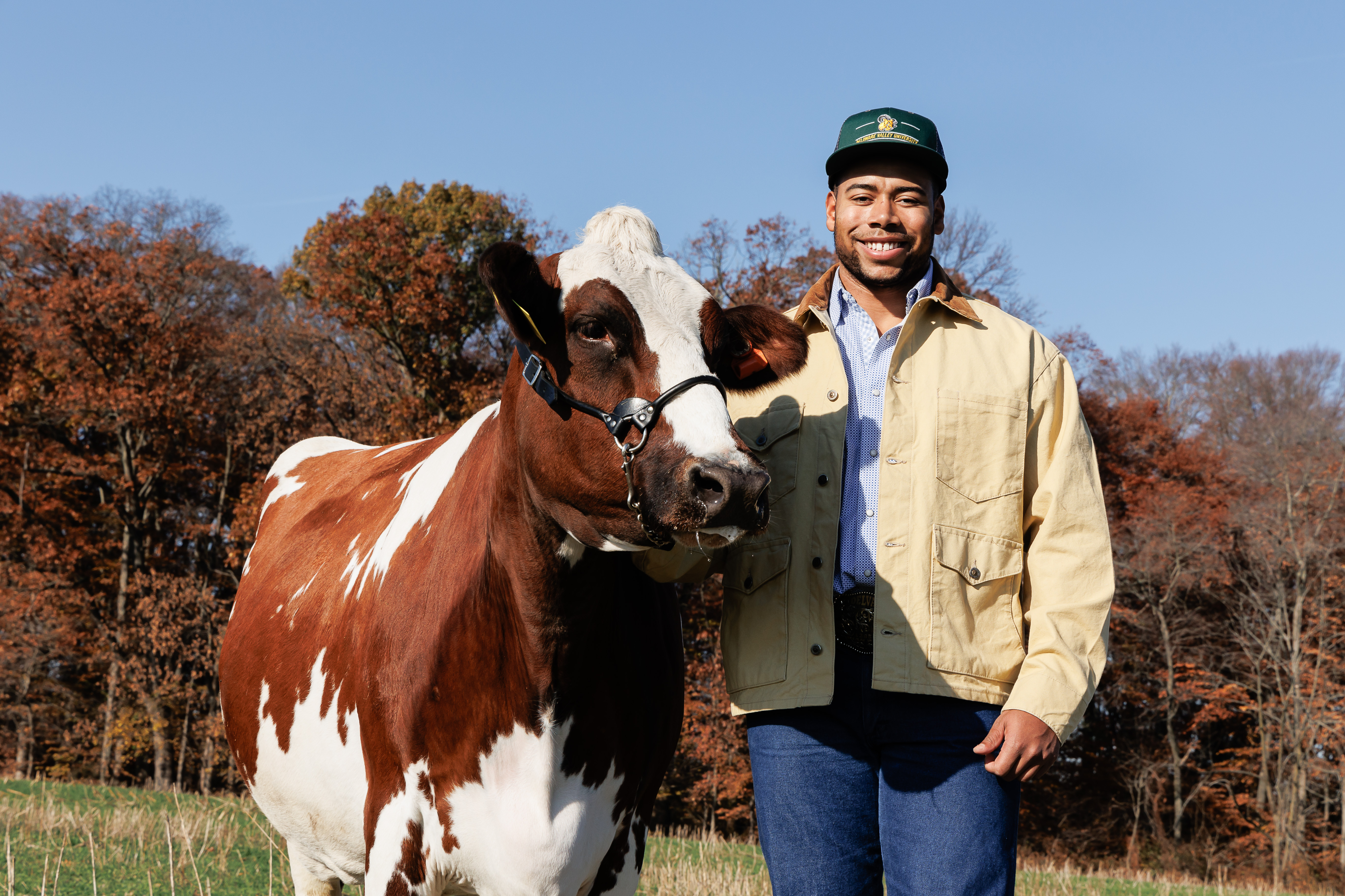 Darian Poles, a previous student is in the fields with a cow beside him. 