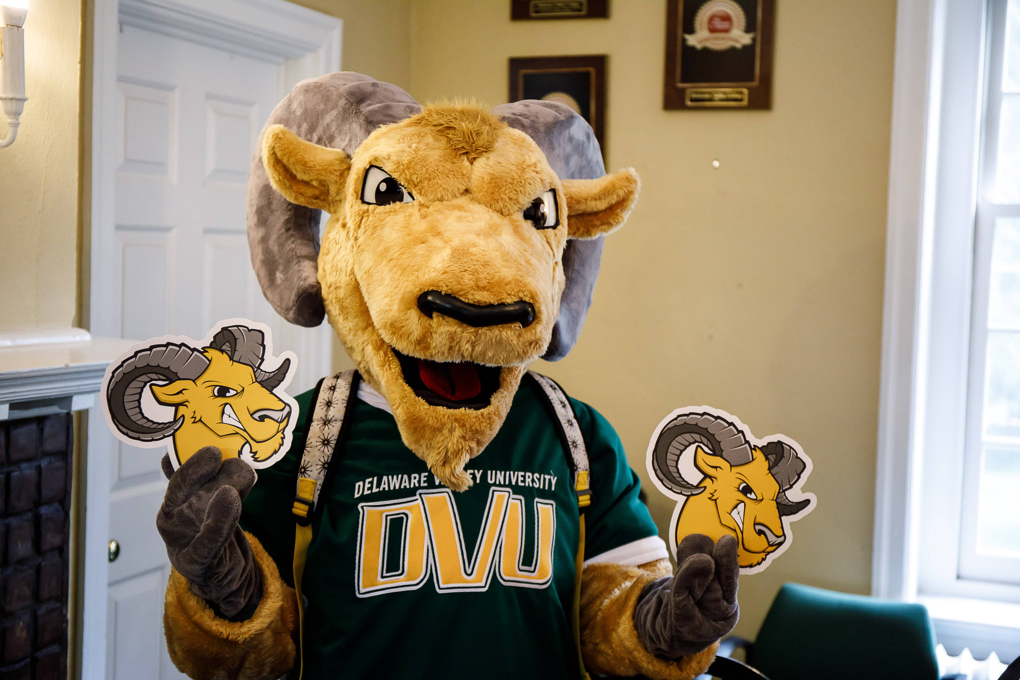 Caesar, the university mascot, is holding two paper cutout of his head, one in each hand. 