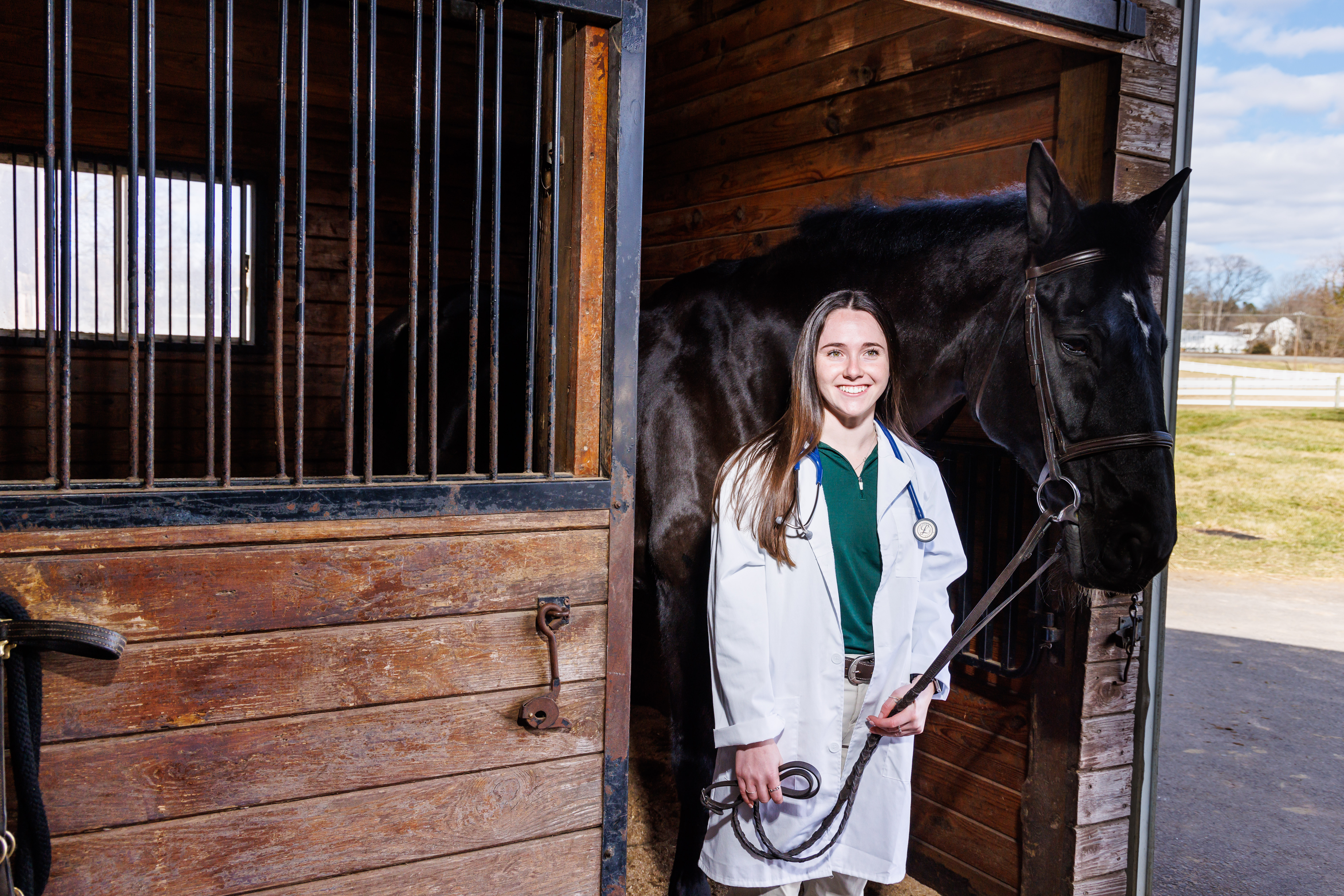 Nina Dellarte with a white coat and a horse in the stables of DelVal.