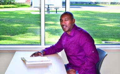 African-American man sitting at table with computer and smiling.