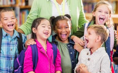 Teacher with large group of children smiling and hugging and wearing colorful clothing.