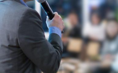 Principal holding microphone and speaking to large group of people 