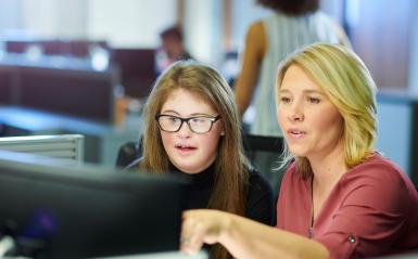Female teacher with teenage girl with Down Syndrome working together at a computer.