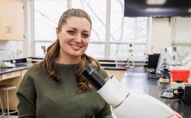 Kimberly Reichner headshot in the lab by a microscope. 