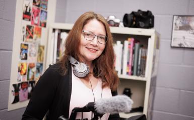 Marion is pictured in the media lab, with headphones and a video camera in hand. 