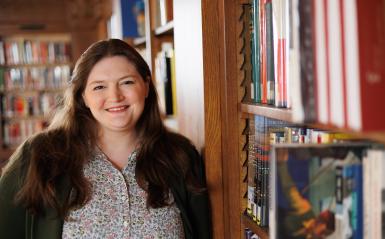 Claire Drolet is standing the library in front of books for a headshot. 