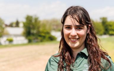 A headshot of jaclyn fiola wearing a delval green collared shirt in a field of soil. 