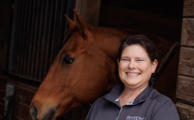 Rebecca Splan Headshot in front of a horse in the equestrian center.