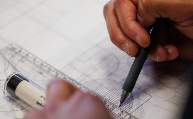 A student is using graphing paper and pencil to draw landscape designs. 