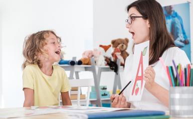 A speech language pathologist is pointing to a paper with letters on it to teach speech techniques.
