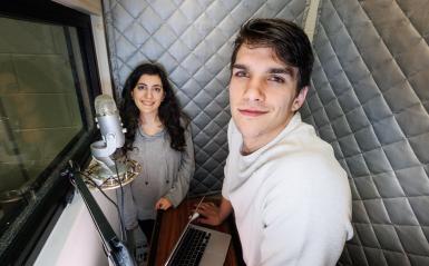 Two students, a male and female, are in the sound booth located in our media lab. 