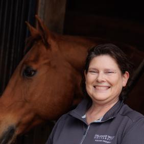 Rebecca Splan Headshot in front of a horse in the equestrian center.