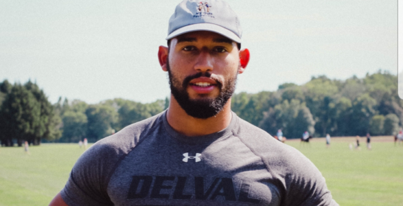 Nigel Feliz wearing a delval tshirt and cap standing on the quad.