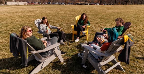 Five students sitting in adirondack chairs in a grass field
