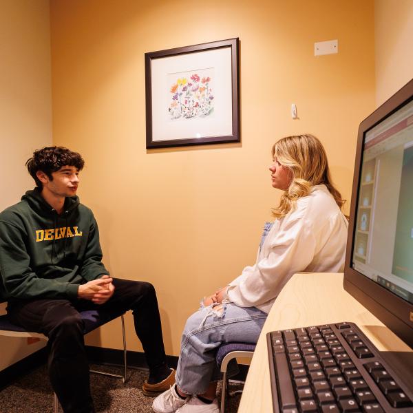 Two students are in the counseling lab speaking with one another. 