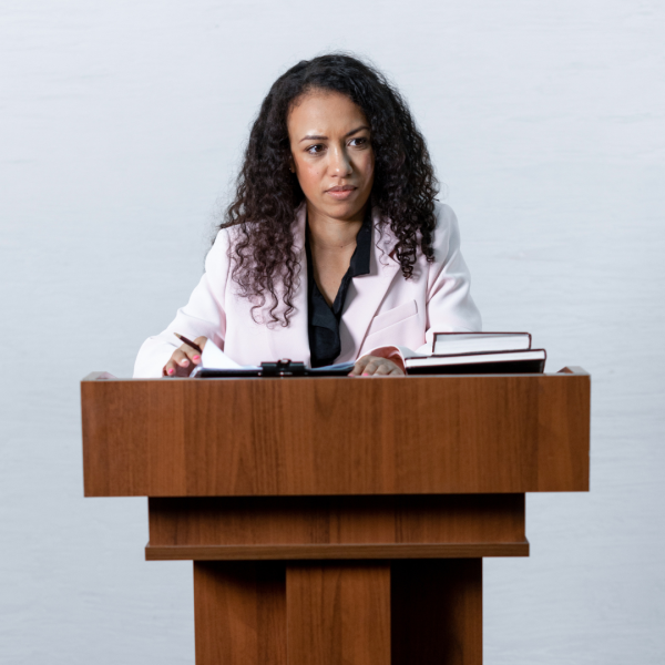 A female in business wear is at a podium looking at an audience. 