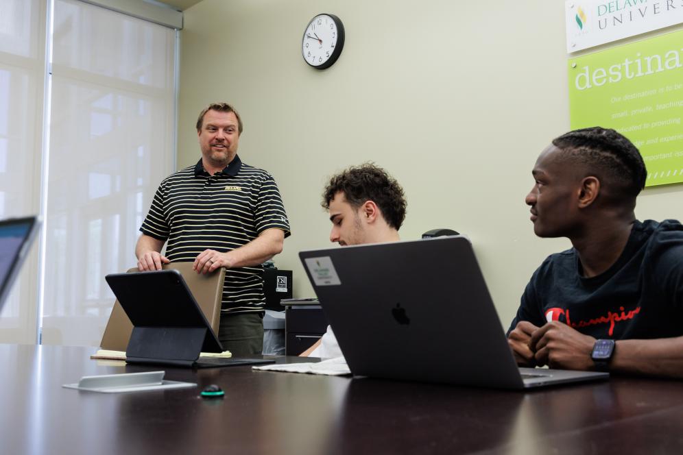 Jeff Wehrung with two students in a conference room having a discussion. 