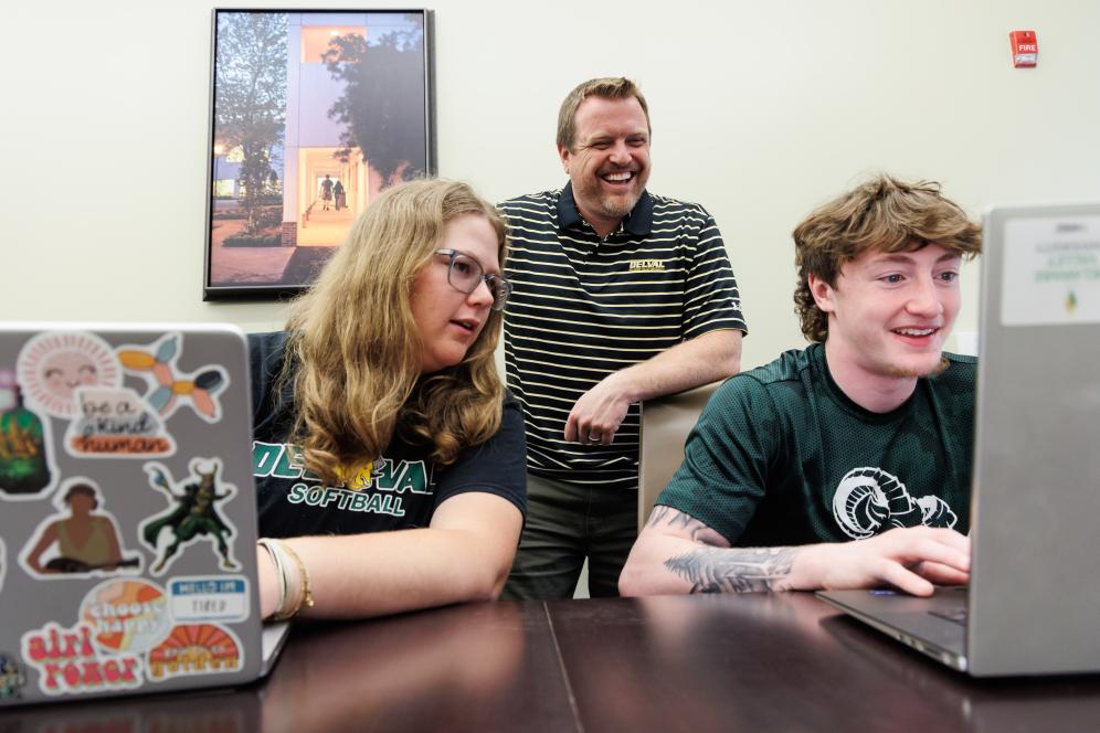 Jeff Wehrung with two students in a conference room having a discussion. 