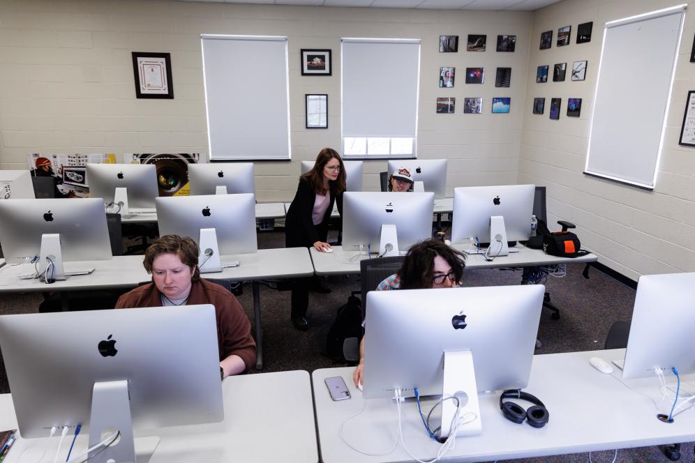 Marion is working with a male student indoors in front of a mac computer. 