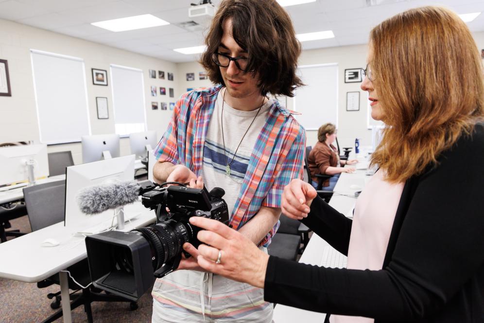Marion is working with a male student indoors with a sony video camera.