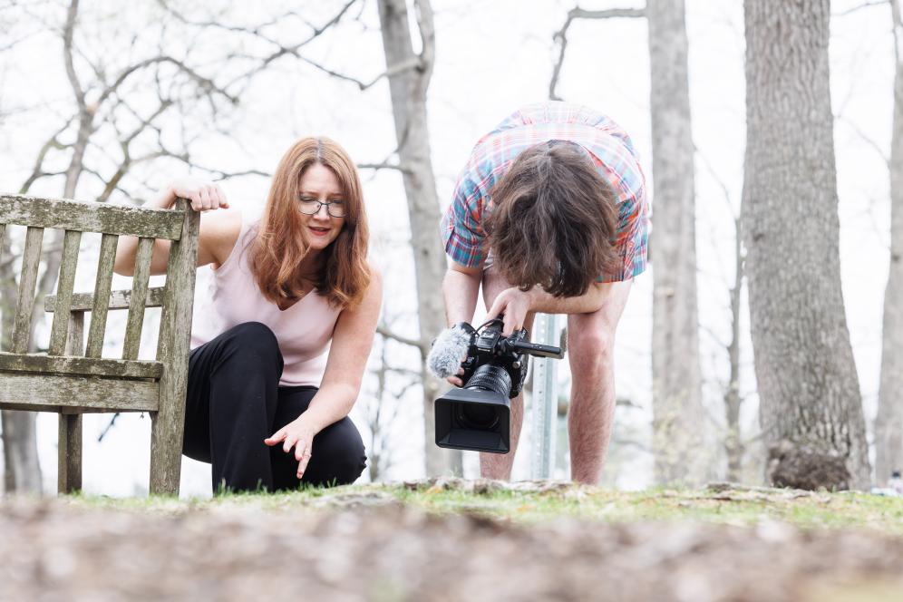 Marion is working with a student outdoors with camera equipment.
