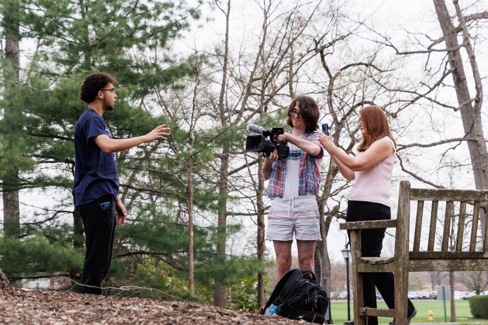 Marion is working with two students outdoors with camera equipment.