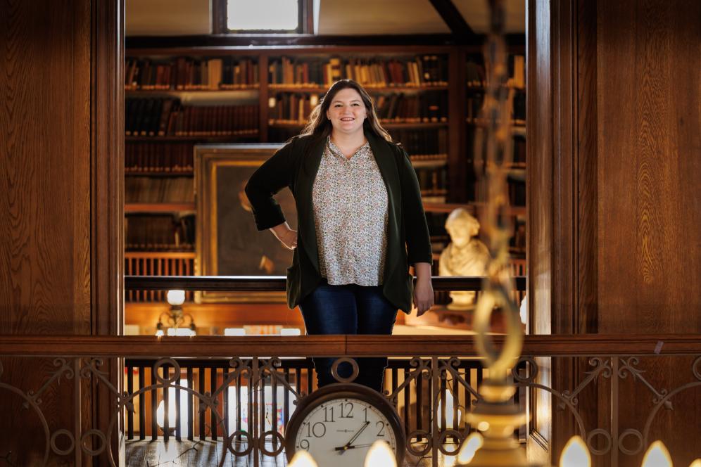 Claire standing in the balcony of the library in front of old archived books. 