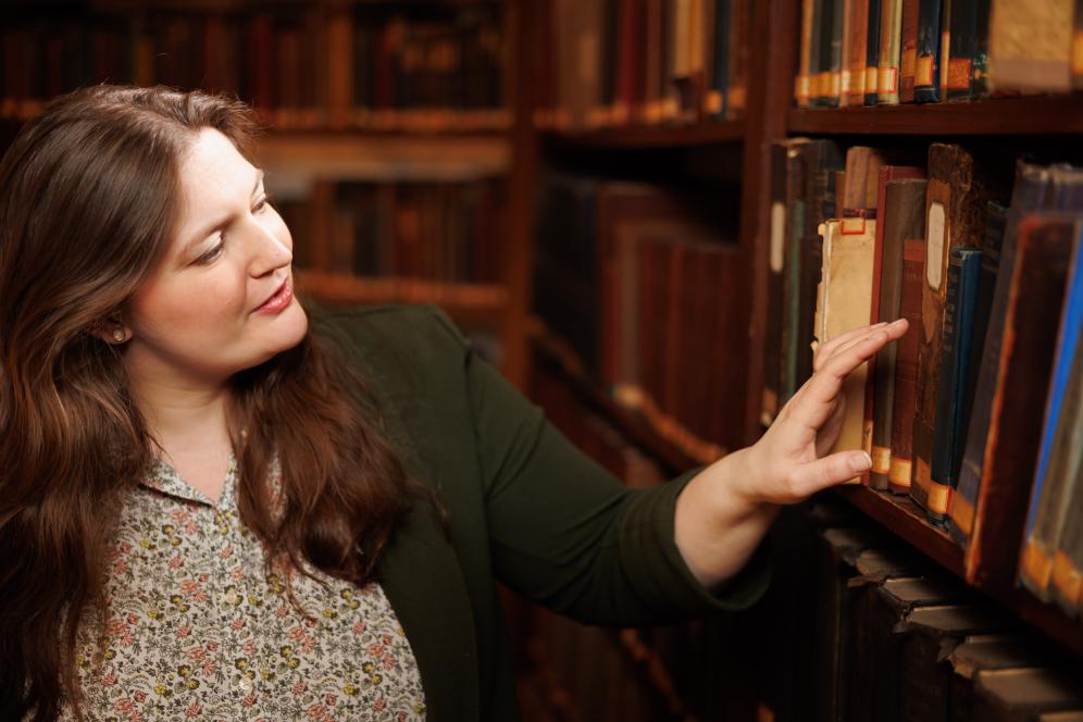 Claire Drolet is pointing at an old book on the shelf in the library. 