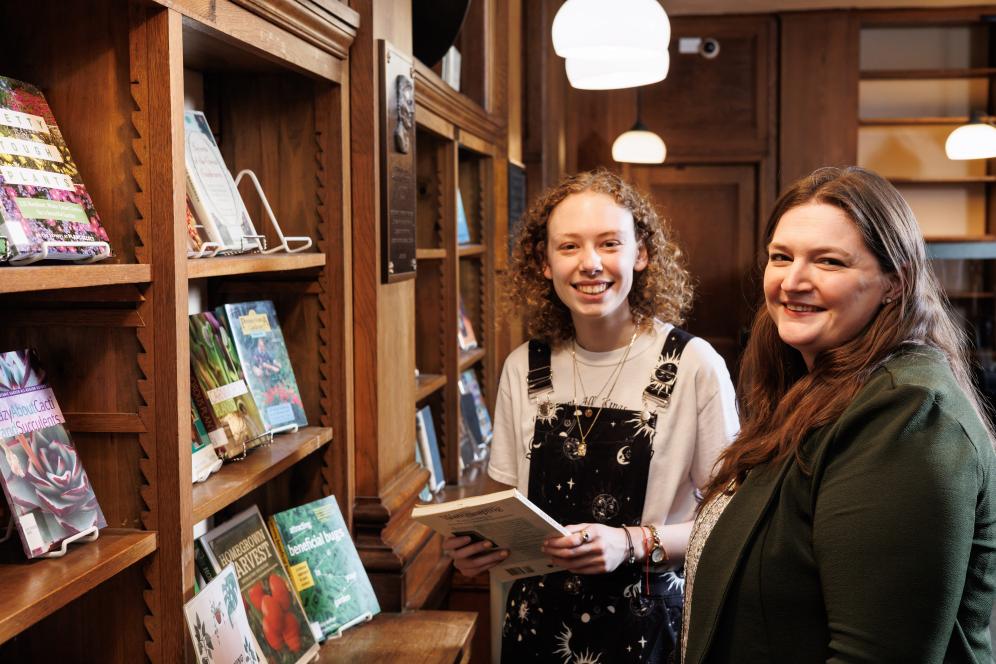 Claire Drolet is working with Jordan Walp in the library in front of a bookshelf. 