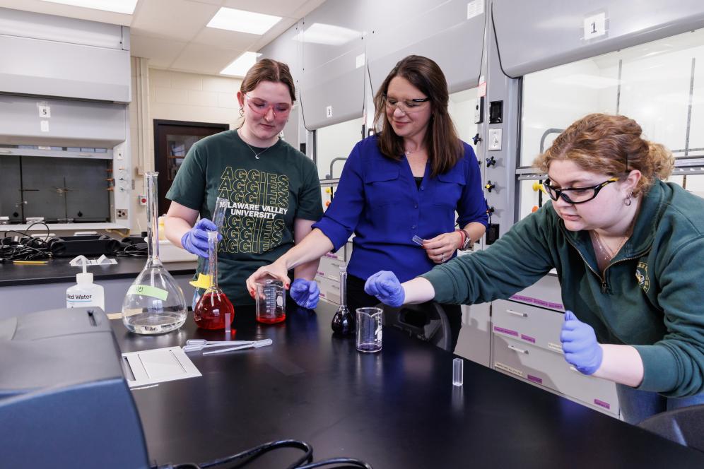 Melissa Langston in the chemistry lab with two students working with beakers. 