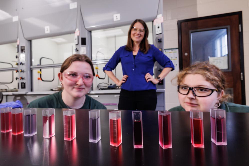 Melissa Langston in the chemistry lab with two students working with beakers. 