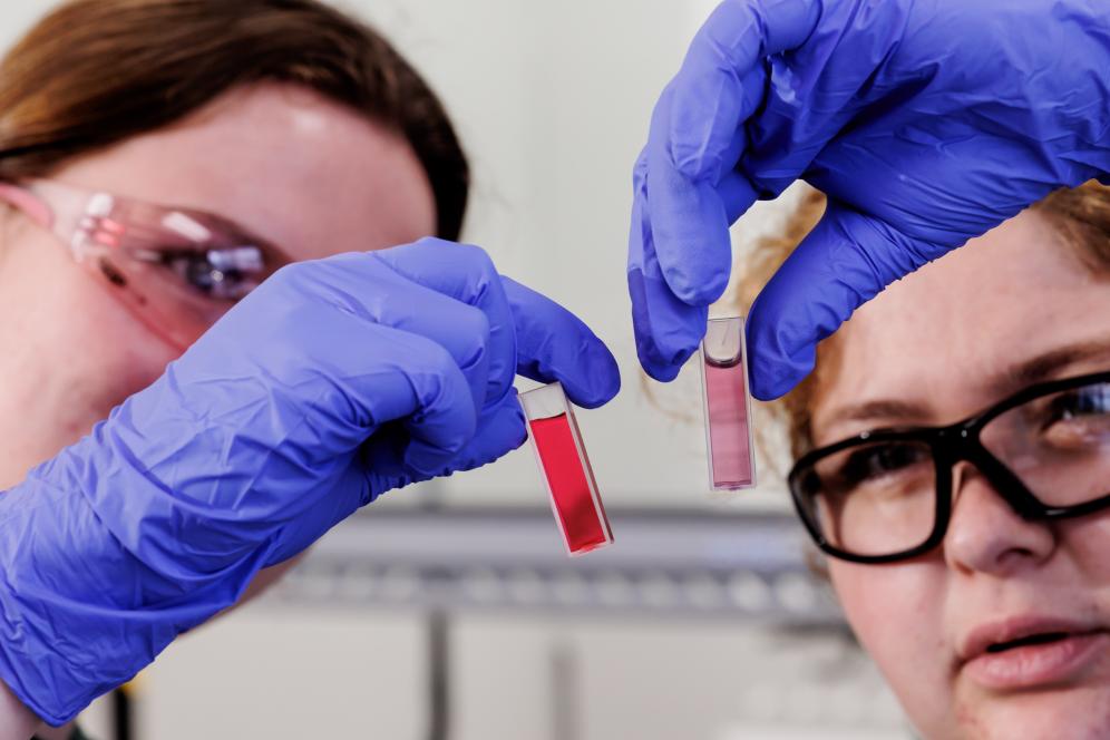 Two students hold up a vile of substances wearing gloves. 