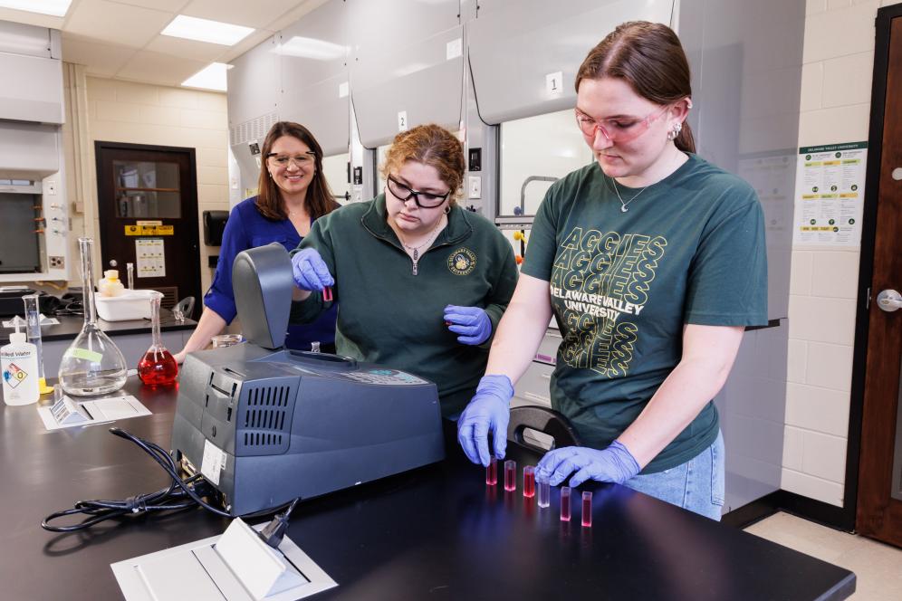 Melissa Langston in the chemistry lab with two students working with beakers. 