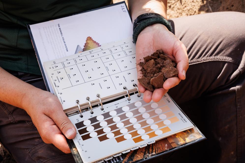Jaclyn is holding a handful of soil next to a color grade scale notebook. 