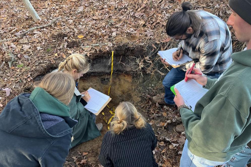 Five students working in a soil pit with notebooks and measurement tools