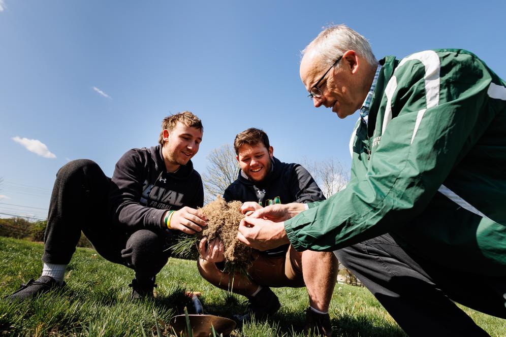 Doug Linde is with students on a field on campus looking at grass samples. 