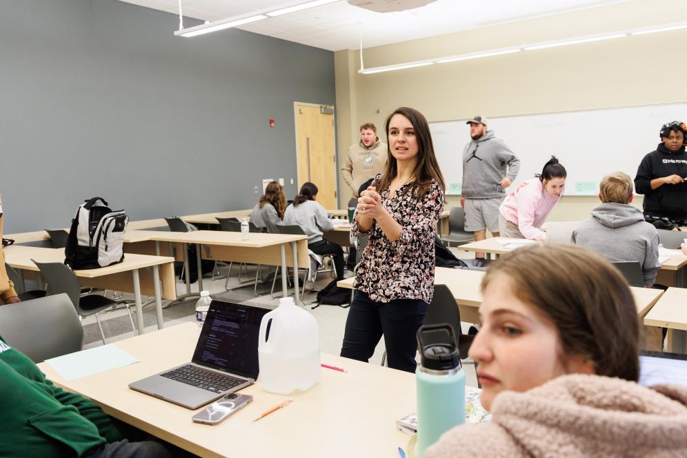 Megan is standing in the middle of a classroom teaching students.