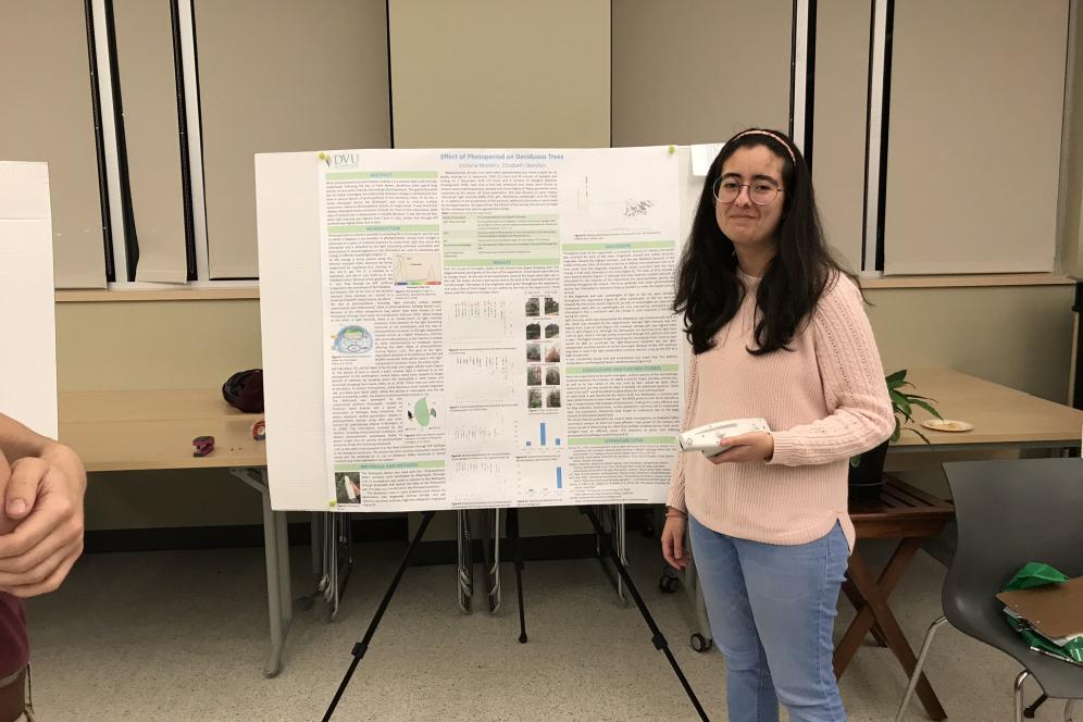 Victoria Moreira, a student, is standing beside her research poster.