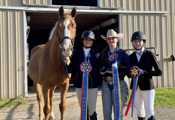 Three students are holding up awards next to a horse. 