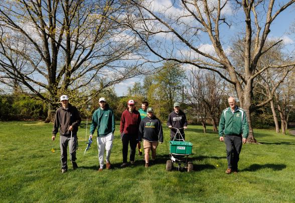 Doug linde is walking with students on a grassy field. 