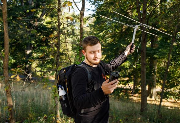 A student is using equipment to test the environment in a wooden area. 