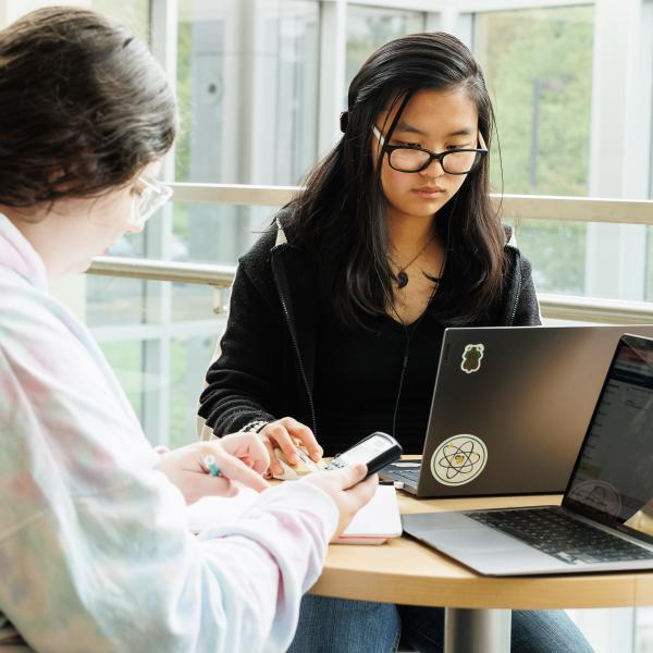 A student wearing glasses is studying next to her friend with her laptop. 