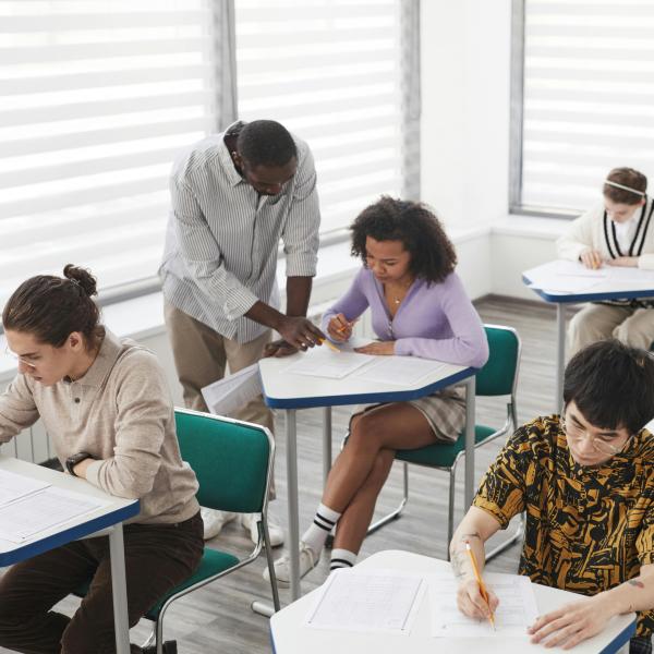 High school students are in a classroom working with a teacher. 