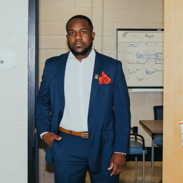 Keith is wearing business attire while standing by a door that has a philadelphia sixers jersey hanging. 