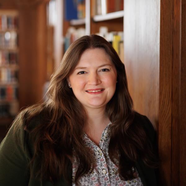 Claire Drolet is standing the library in front of books for a headshot. 
